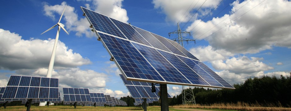 Solarpanels und Windrad auf der grünen Wiese montiert, vor blauem Himmel mit weißen Cumulus-Wolken